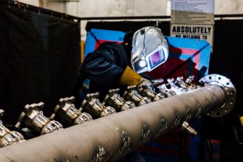 A welder working on a prefabricated piping assembly.